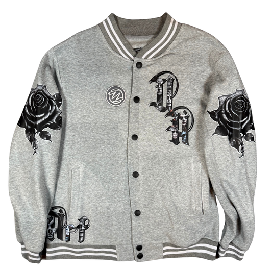 Front view of grey varsity bomber jacket with UA Day of the Dead letter artwork, black rose sleeves, front pockets, and snap-button closure.