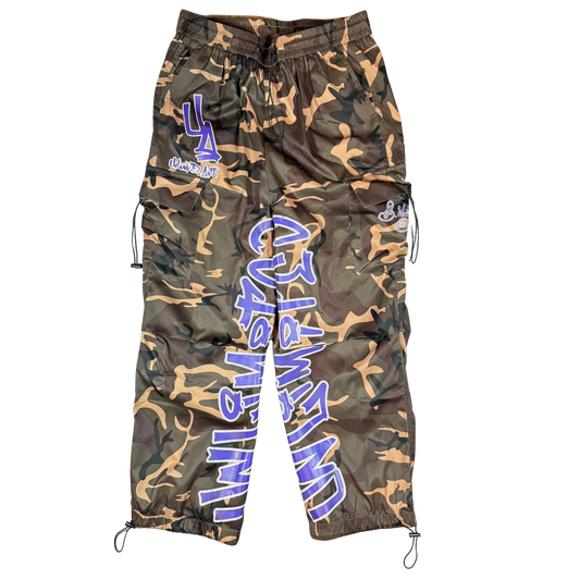 Back view of loose-fit camo cargo pants with oversized blue and white Unlimited Arts graffiti lettering down the leg and utility pockets.