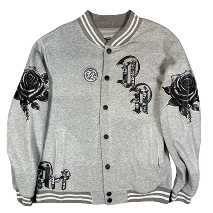 Front view of grey varsity bomber jacket with UA Day of the Dead letter artwork, black rose sleeves, front pockets, and snap-button closure.