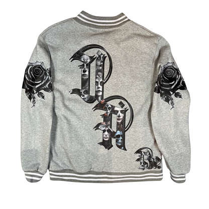 Back view of grey bomber jacket featuring oversized gothic UA letters filled with Day of the Dead artwork and black rose graphics on each sleeve.