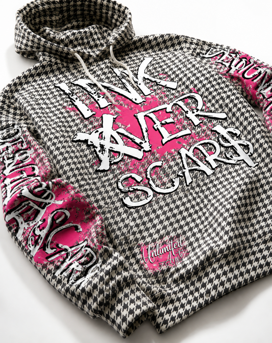 A black and white houndstooth hoodie featuring a large white graphic text overlay reading 'INK OVER SCARS' with a bright pink paint splatter background, and a small pink, ‘Unlimited Art' logo near the lower front. Designer Scars written down the sleeve