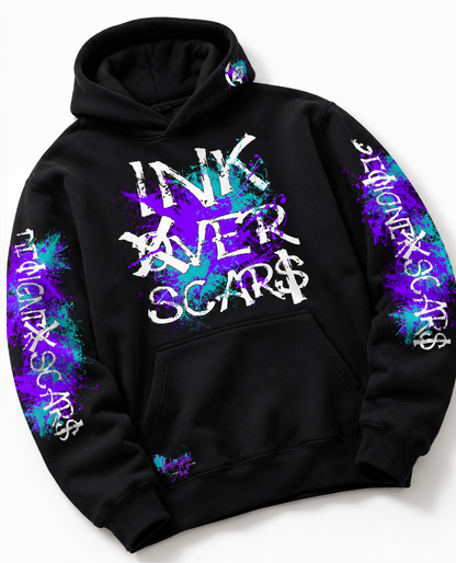 A black pullover hoodie with a front kangaroo pocket, featuring a large distressed white graphic on the chest that reads 'INK OVER SCAR$' over a purple and blue paint splatter design. The sleeves also feature vertical white text reading 'INK OVER SCAR$' integrated with matching purple and blue splatters.
